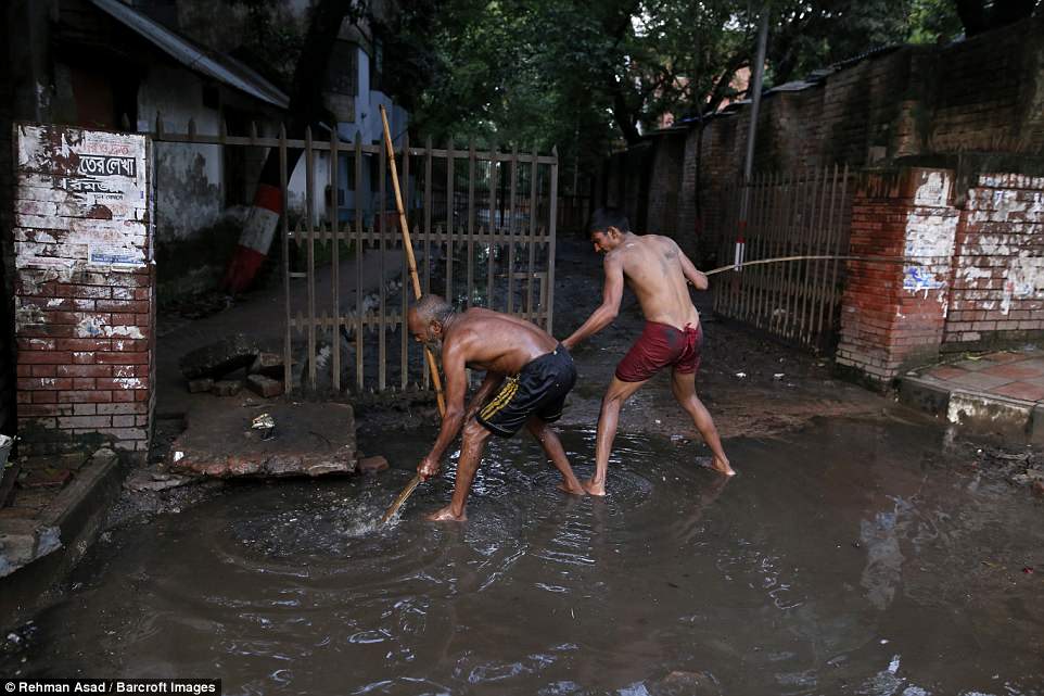A pair of cleaners try to clear a blockage with a long stick so they don't have to dive back into the murky waters