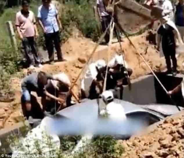 Video footage of the bizarre service shows the silver saloon bearing the body of the man being slowly lowered into a large grave by an excavator
